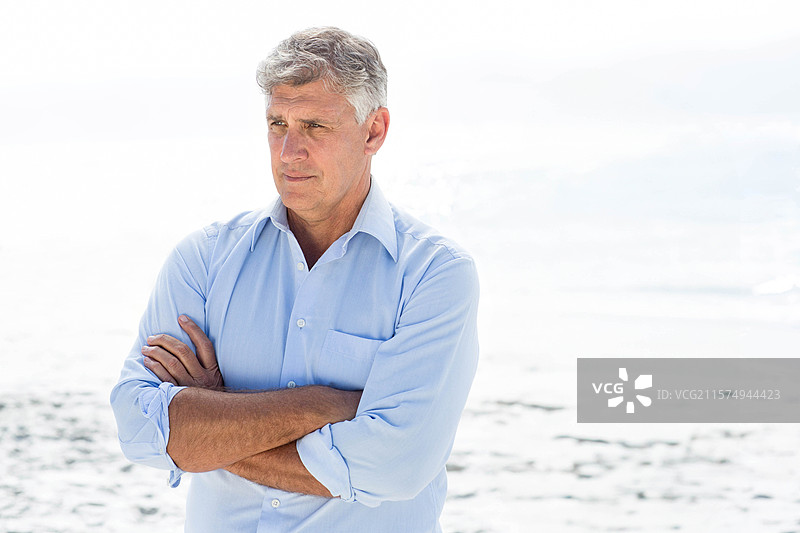 中年男子站在沙滩上，卷起衬衫袖子，凝视着大海，留有空白空间图片素材