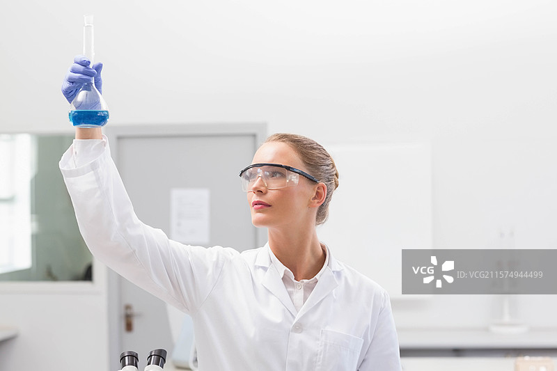 一个装有蓝色溶液的锥形瓶静静地放在明亮实验室的实验台上，旁边是显微镜。图片素材