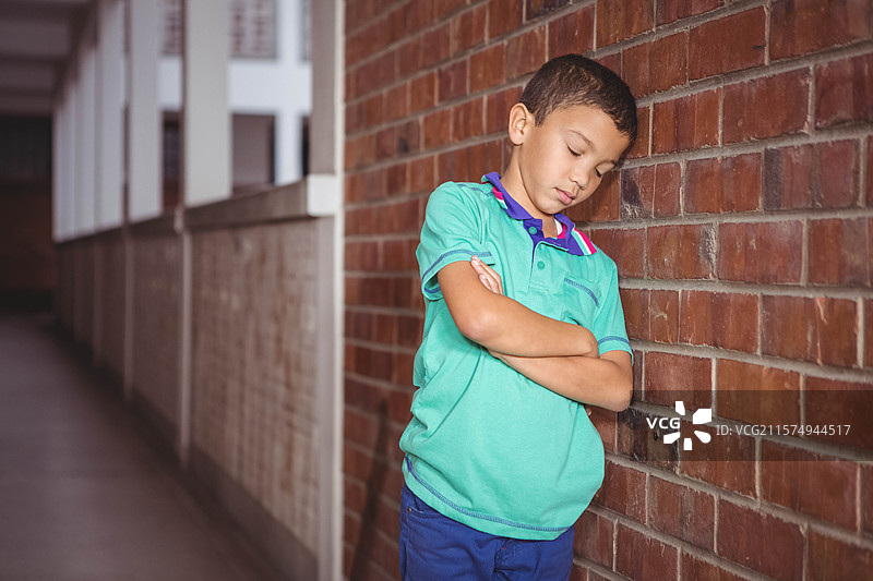 男孩靠在红砖墙和白色栏杆上，双臂交叉，站在走廊里，有空白空间。图片素材