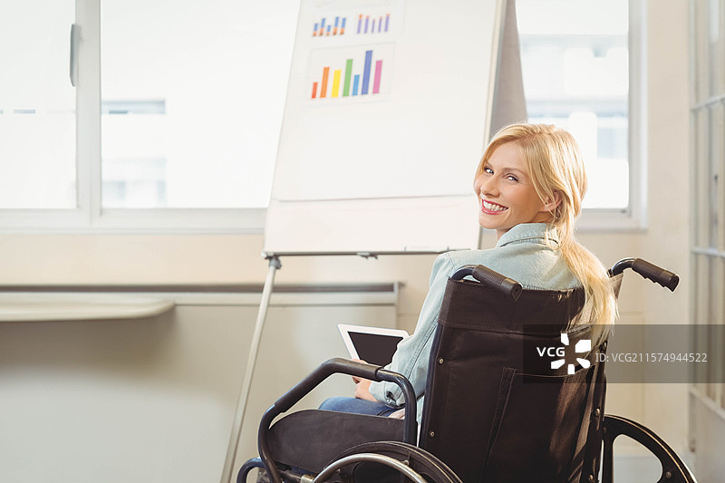 在办公室里，坐在轮椅上的女性手持平板，指着窗边的翻转图表，旁边留有空白空间。图片素材