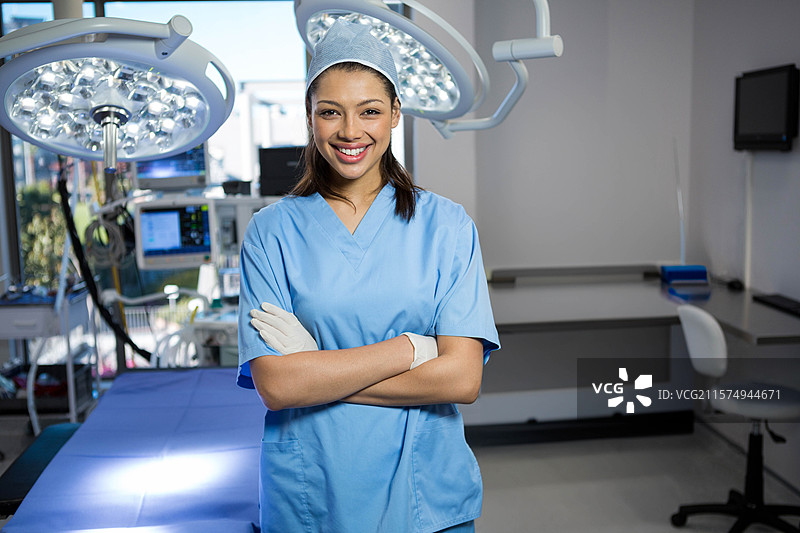 穿着手术服的女性外科护士站在手术室的桌子头部，灯光下。图片素材