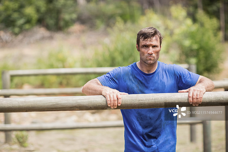 男子在森林空地上穿着蓝色衬衫，抓住木梁进行障碍训练图片素材