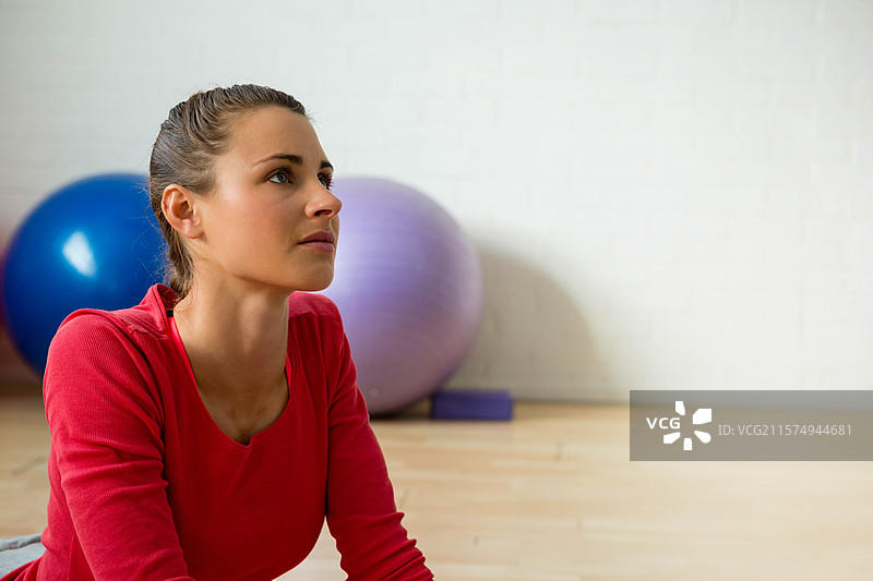 二十多岁的女性坐在瑜伽工作室的木地板上，旁边有稳定球和瑜伽砖。图片素材