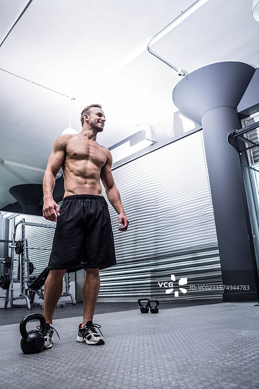 男性在健身房的金属墙壁和架子上，使用纹理垫进行壶铃锻炼，留有空白空间。图片素材