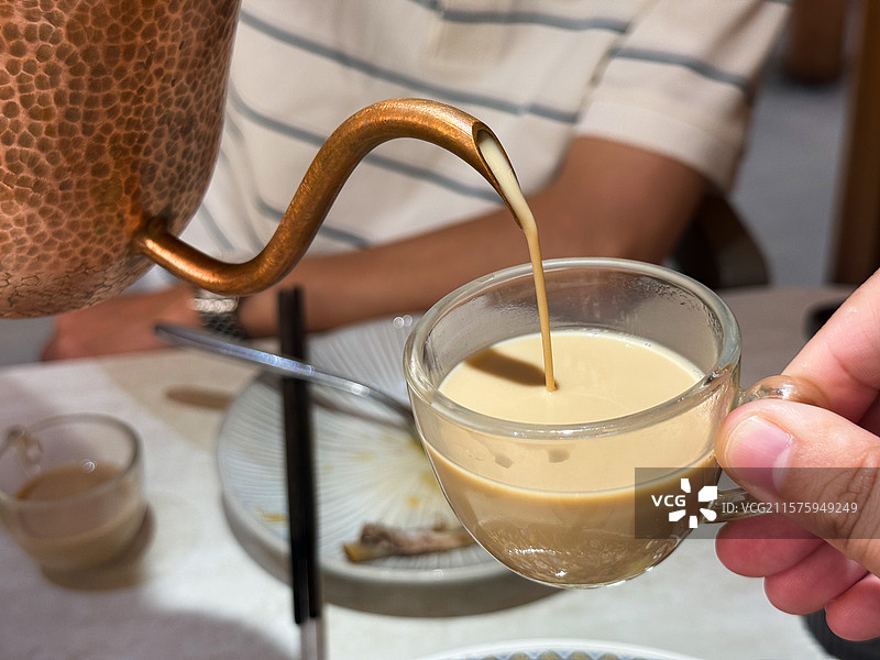 从铜壶往杯子中倒奶茶特写，新疆奶茶图片素材