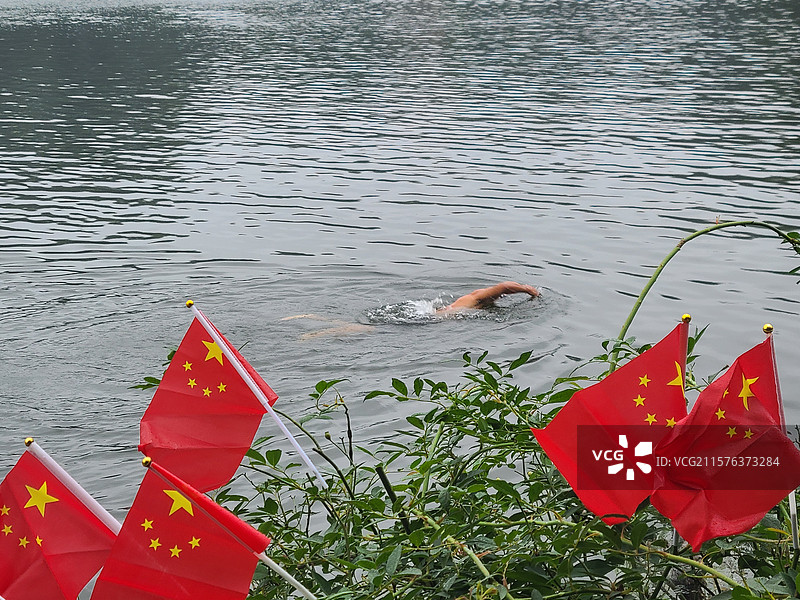 南京明孝陵景区里面山顶上有个美丽的紫霞湖，像天池，一个人正在湖里游泳，岸边红旗招展为他加油图片素材