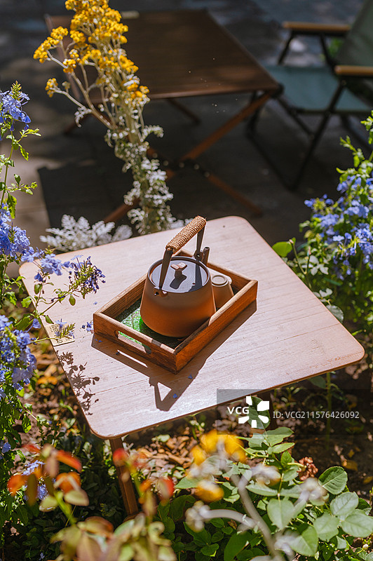 花园中洒满阳光的木桌上托盘中的陶制茶壶 悠闲的田园风格图片素材