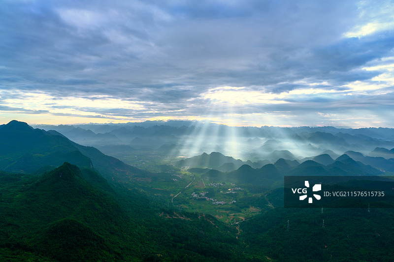 清晨的阳光穿透云层投射在喀斯特地貌的山峰上图片素材