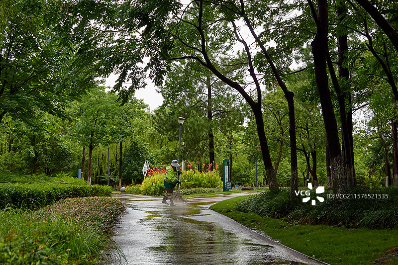 雨后公园树荫下，环卫工人正在清扫积水，绿色环境映衬下显得格外宁静图片素材