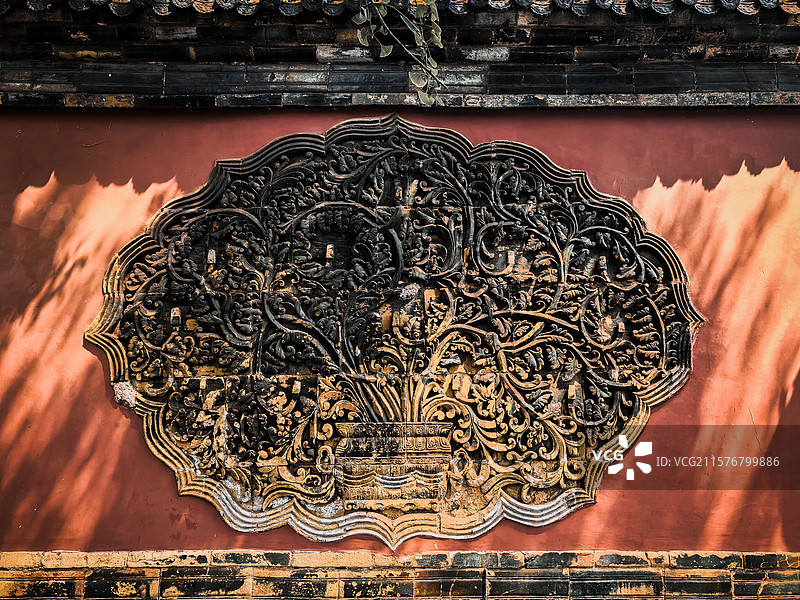 寺庙的红墙，墙上有一块精美的雕刻装饰，光影交错，给人一种庄重而古朴的感觉图片素材