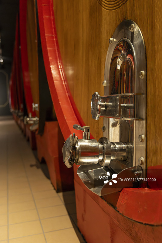 酒窖中大型橡木酒桶及其金属出酒口装置特写图片素材