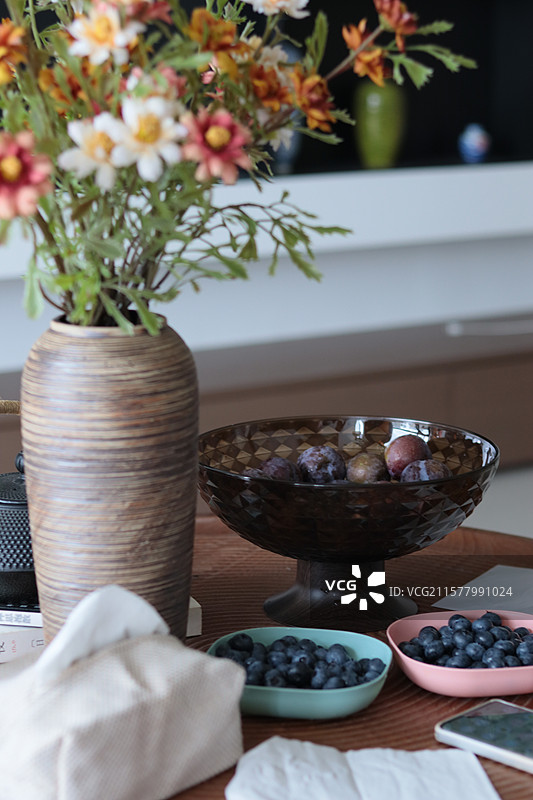 花瓶里的花、蓝莓、李子在木质桌子上的特写图片素材