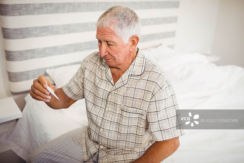 男人坐在床边，查看卧室中带条纹床头板的温度计显示。图片素材