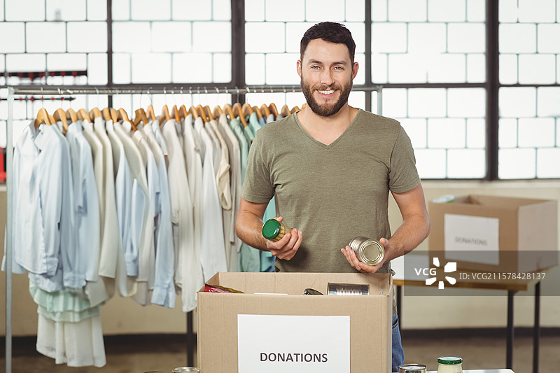 志愿者在捐赠中心的衣架和捐赠箱旁整理罐头食品图片素材