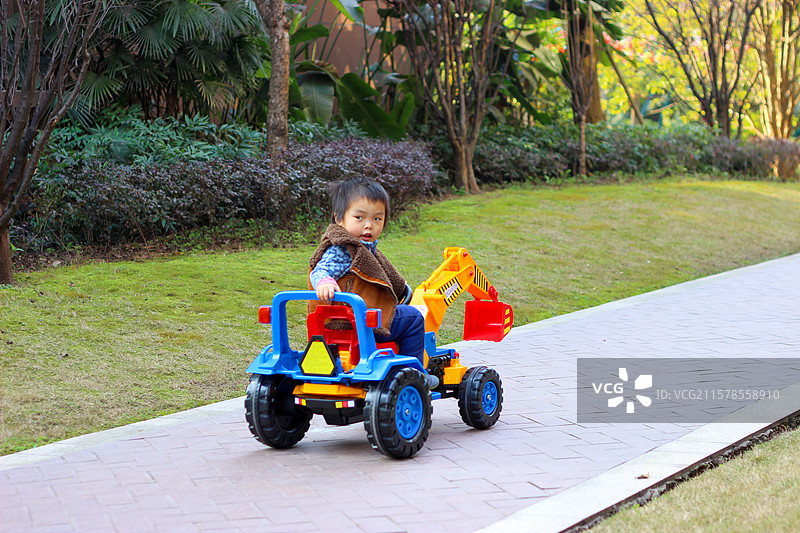 四岁小男孩驾驶着玩具挖掘机在小区内玩耍图片素材