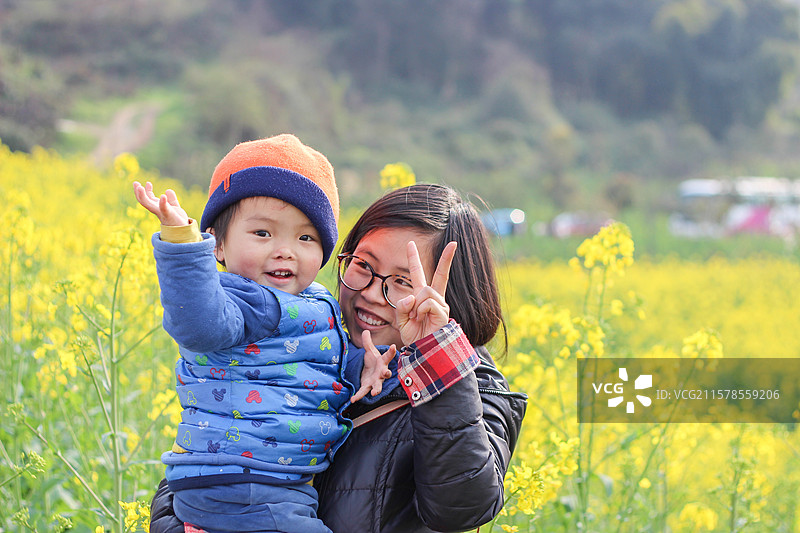 两岁的小男孩在母亲怀抱里踏青观赏油菜花图片素材