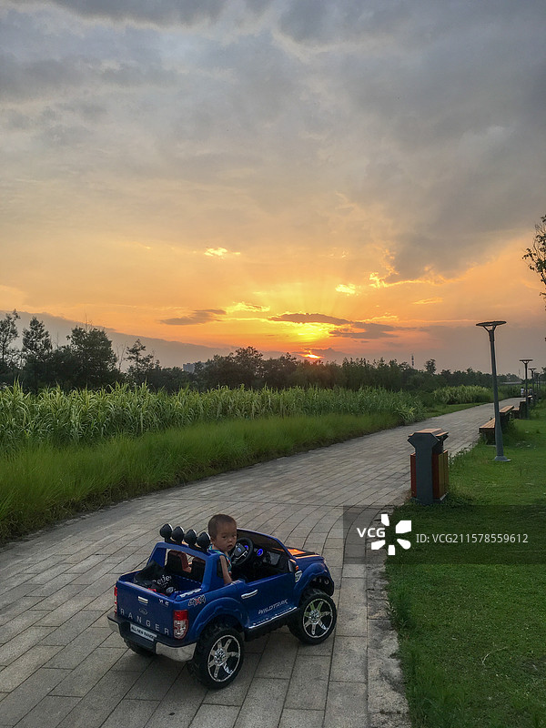 夕阳下的一岁小男孩在公园里驾驶着儿童车游玩图片素材