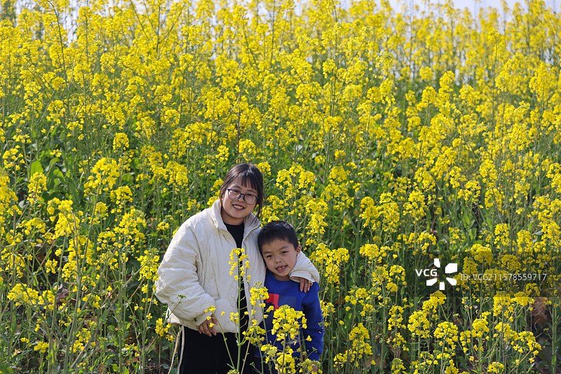 母亲和七岁的儿子在油菜花丛中拍照打卡图片素材