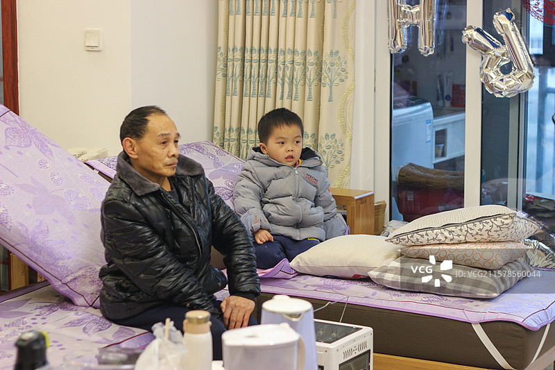 五岁小男孩和舅公一起坐在客厅沙发看电视图片素材