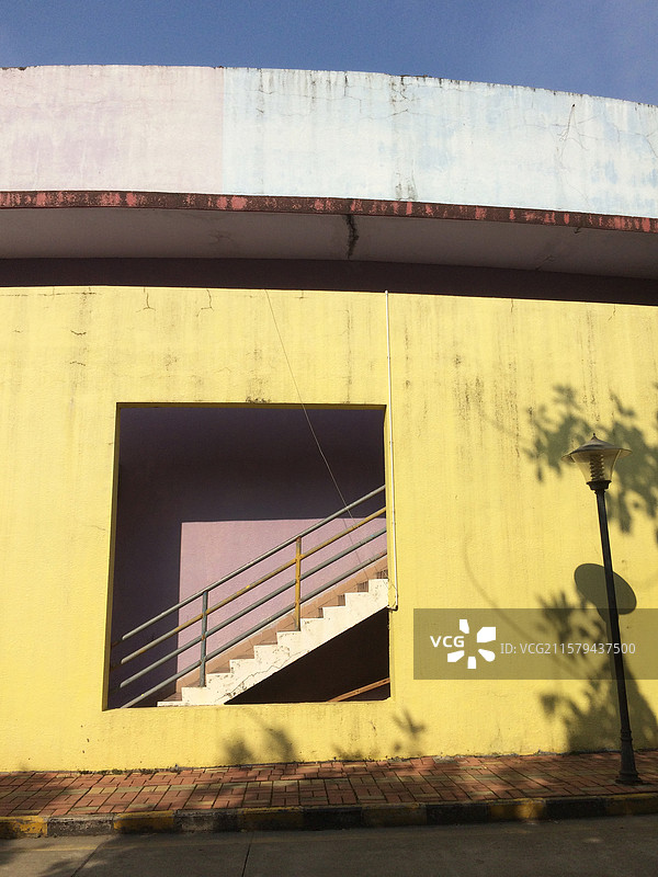路边黄色墙体上一个镂空窗户里面有楼梯图片素材