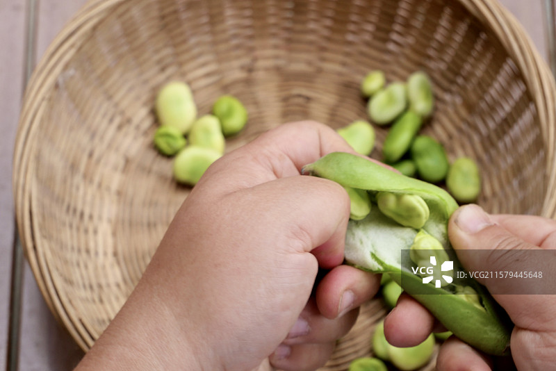 手剥蚕豆荚与竹篮中的蚕豆粒图片素材
