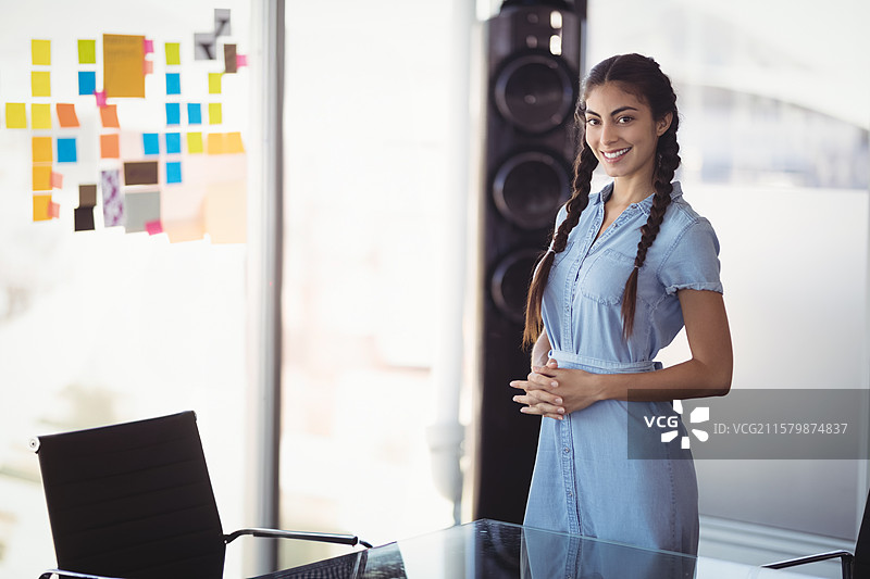 女性专业人士站在玻璃桌旁，桌上有五颜六色的便签和扬声器，身处办公室。图片素材