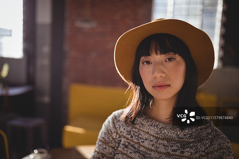 亚洲女性坐在阁楼休息室，戴着棕色帽子和灰色毛衣，手里拿着陶瓷杯，留白空间图片素材