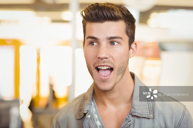 二十多岁的男子在明亮的开放式办公室里，惊讶地交谈，温暖的顶灯照耀着他。图片素材