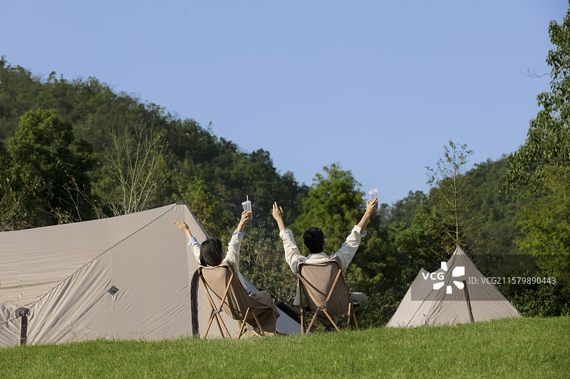 背对着镜头坐在帐篷前休闲聊天的年轻情侣图片素材