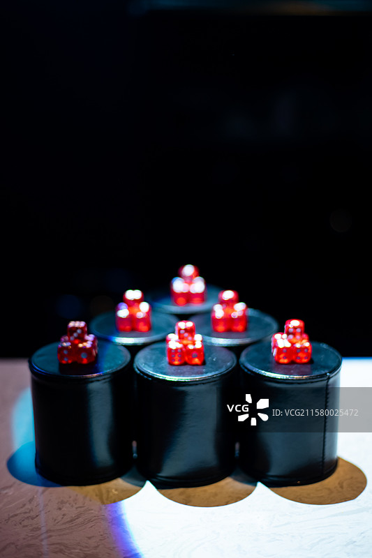 中国休闲娱乐拍摄主题，KTV桌子上上成一排黑色的皮革杯子和一堆红色的骰子，室内无人图像摄影图片素材