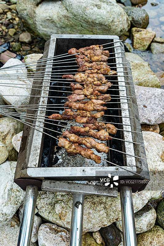 中国饮食产业拍摄主题，一个人手里拿着一把羊肉串在烤炉上烧烤，户外白昼无人图像摄影图片素材