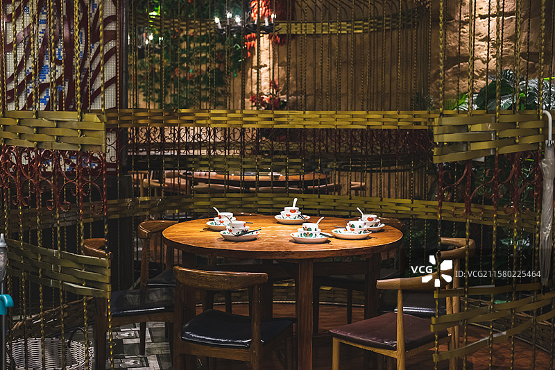 中国餐饮餐厅饭店饭馆行业，空的餐桌拍摄主题，巨大的铁质鸟笼里木制圆桌上的餐具，室内无人图像摄影图片素材