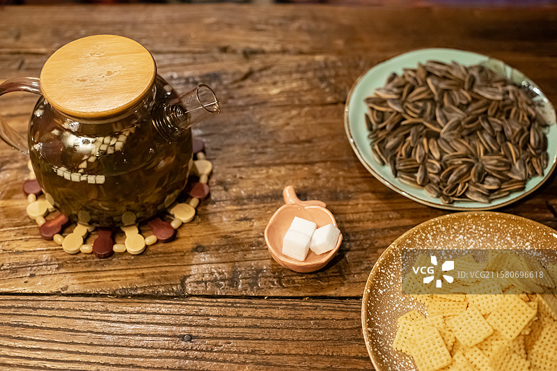 中国休闲娱乐健康生活方式拍摄主题，木制桌子上一堆黄色的锅巴瓜子小吃暖水壶和玻璃杯，室内无人图像摄影图片素材