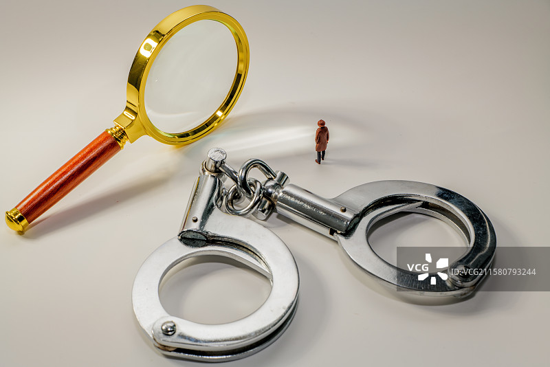 白色背景下放大镜手铐和模型小人的高角度视图图片素材