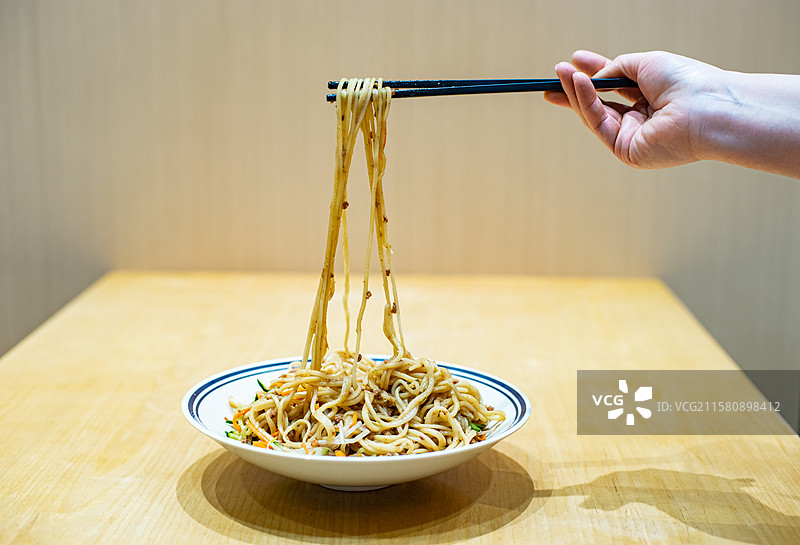 中国餐饮行业饮食产业，传统经典中国食品，筷子拉起一盘子北京炸酱面，室内人手图像图片素材