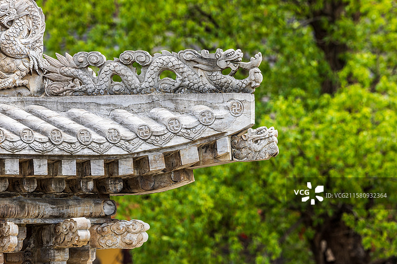 传统建筑屋檐上的精美龙形雕刻和吉祥图案，背景是茂密的绿树，展现出东方文化的艺术魅力。图片素材