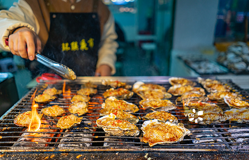 中国餐饮行业饮食产业传统经典中国食品，美食拍摄主题，铁丝网烤肉架上的烧烤生蚝特写，户外夜晚无人图像图片素材