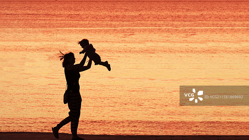 母亲在黄昏河边举起孩子图片素材