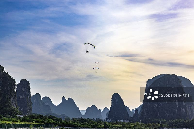 黄昏滑翔伞在桂林阳朔的高空飞行，桂林阳朔一座座山与空中的滑翔伞，喀斯特地貌地区的滑翔伞飞行运动图片素材