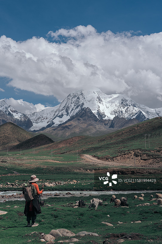 手持转经筒的牧羊人和溪流边吃草的羊群图片素材