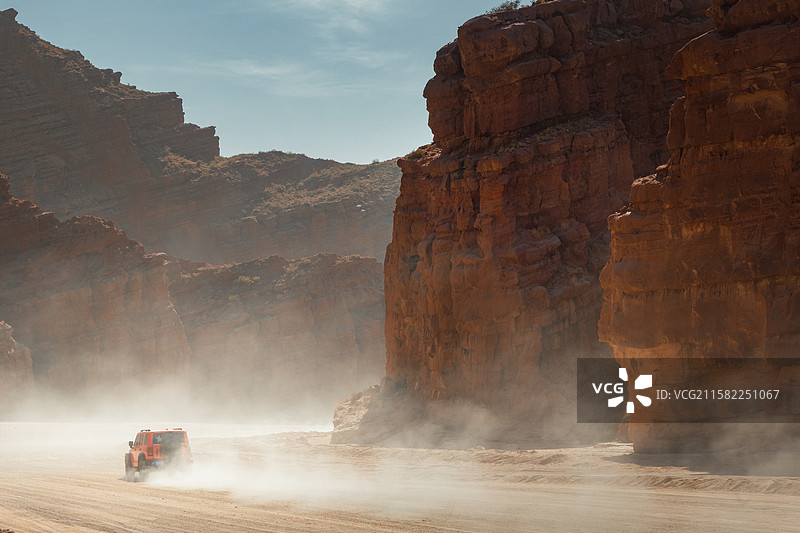赤岩环抱的温宿大峡谷间，扬尘如纱幕漫卷，红色越野车破雾而来，绝尘之势劈开万古沉寂图片素材