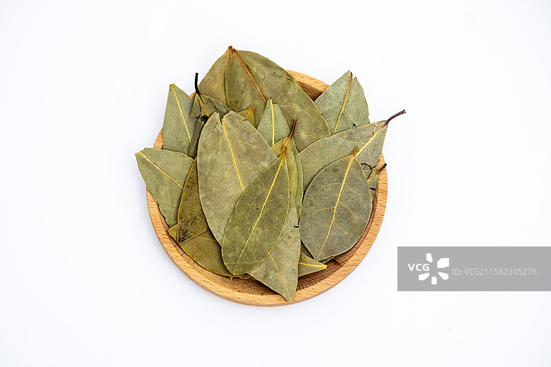 白色背景中木盘子里装着晾晒干的香叶叶子调料图片素材