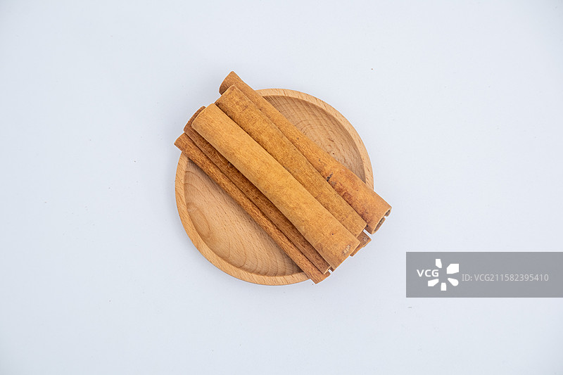 白色背景中木盘子里装着晾晒干的肉桂桂皮调料图片素材