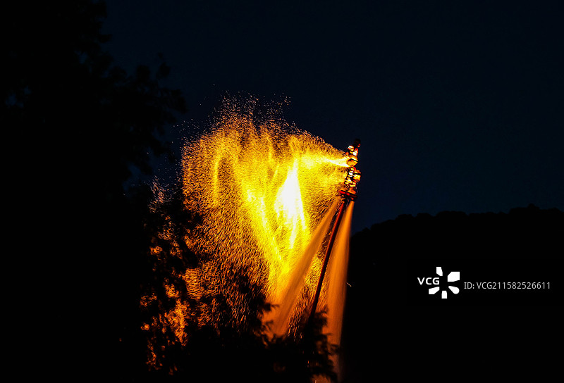 夜晚树丛后的火焰喷射表演图片素材