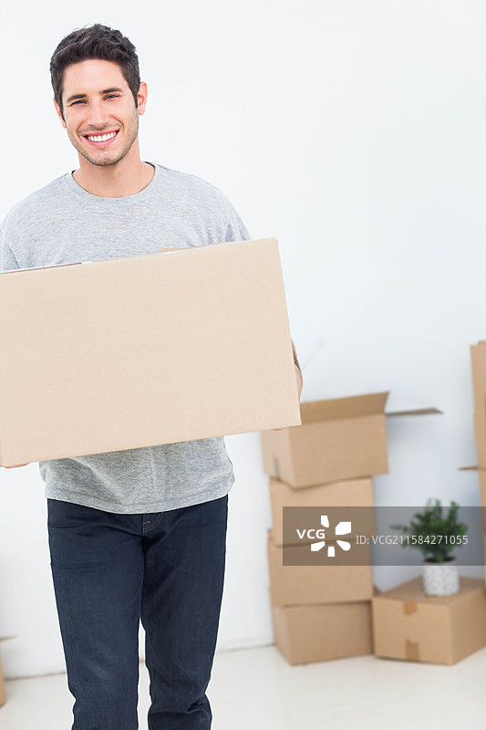 男人在空房间里拿着一个密封的纸箱，周围有搬家的箱子和一盆植物，留有空白空间图片素材