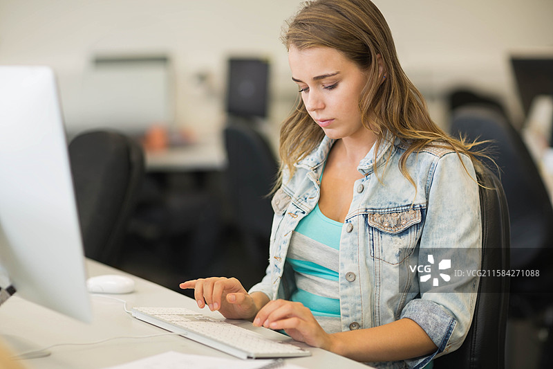 穿着牛仔夹克的女性在共享办公室工作区打字并使用鼠标图片素材