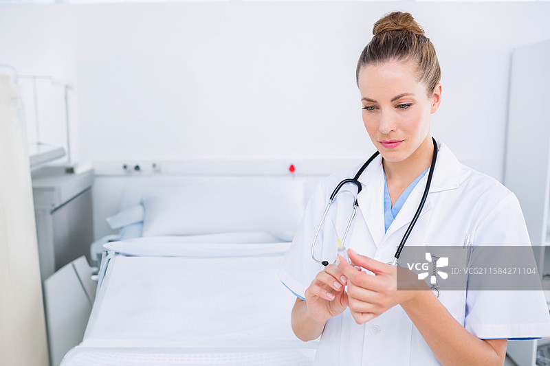 护士在医院病房内准备注射器，身穿白大褂，床边和柜子旁，有空白空间。图片素材