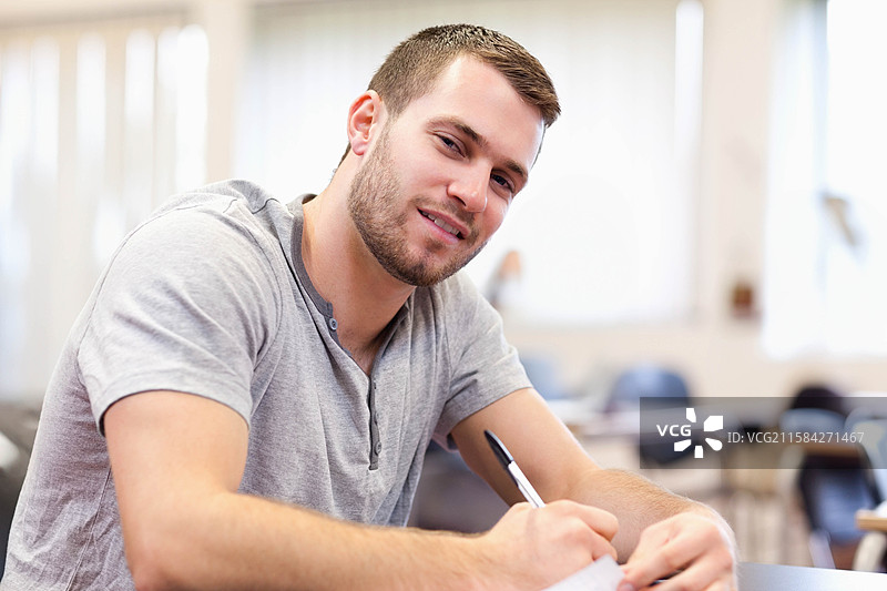 学生在教室的书桌上用笔在纸上写字，窗外柔和的光线透进来。图片素材