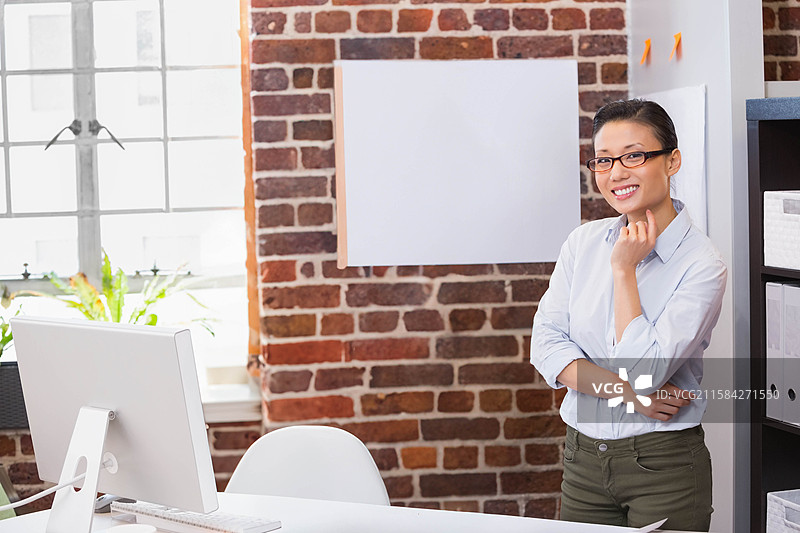 中国女性站在砖墙办公室桌旁，正在检查电脑显示器和键盘。图片素材