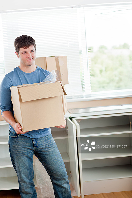 三十多岁的男人穿着衣服，手里拿着装有包装材料的搬家箱子，家中有空白空间。图片素材